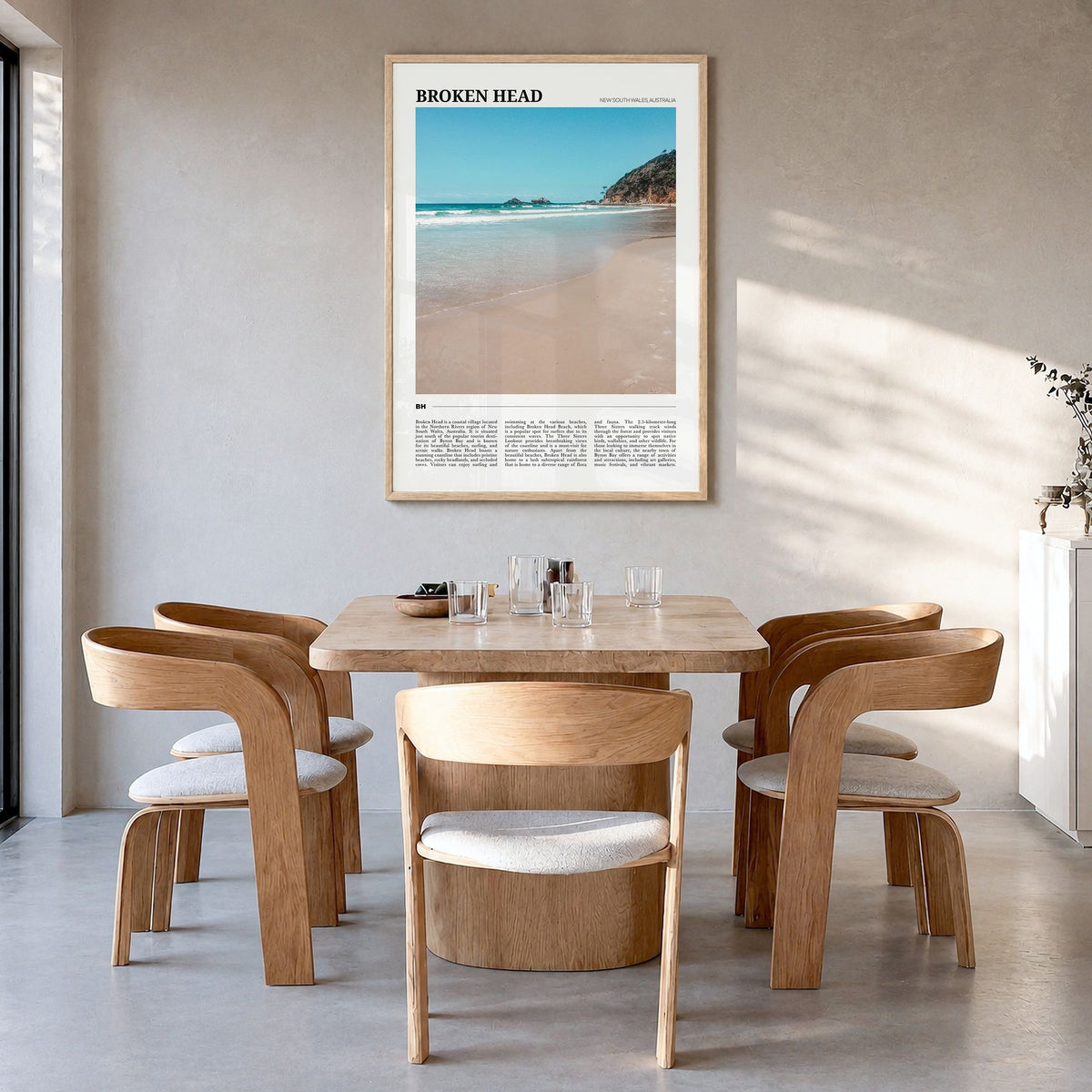 Broken Head Travel Poster in a natural wood frame, hanging in a dining room