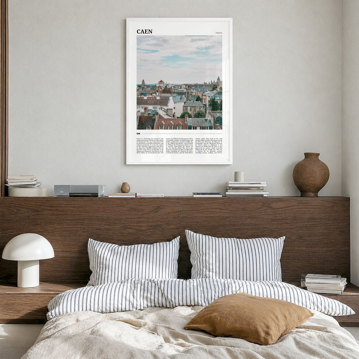 Caen Travel Poster in a white wood frame, hanging in a bedroom