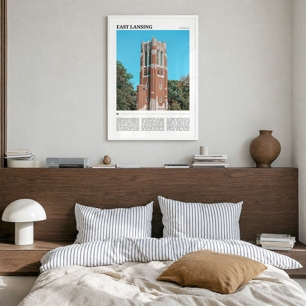 East Lansing Travel Poster in a white wood frame, hanging in a bedroom