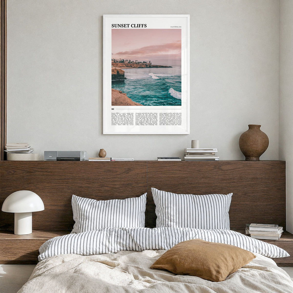 Sunset Cliffs Travel Poster in a white wood frame, hanging in a bedroom