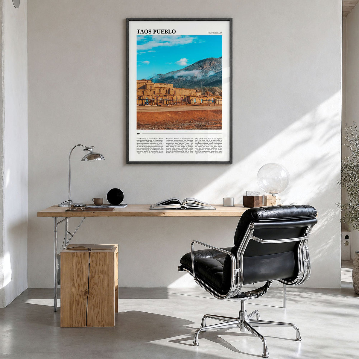 Taos Pueblo Travel Poster in a black wood frame, hanging in a bright home office