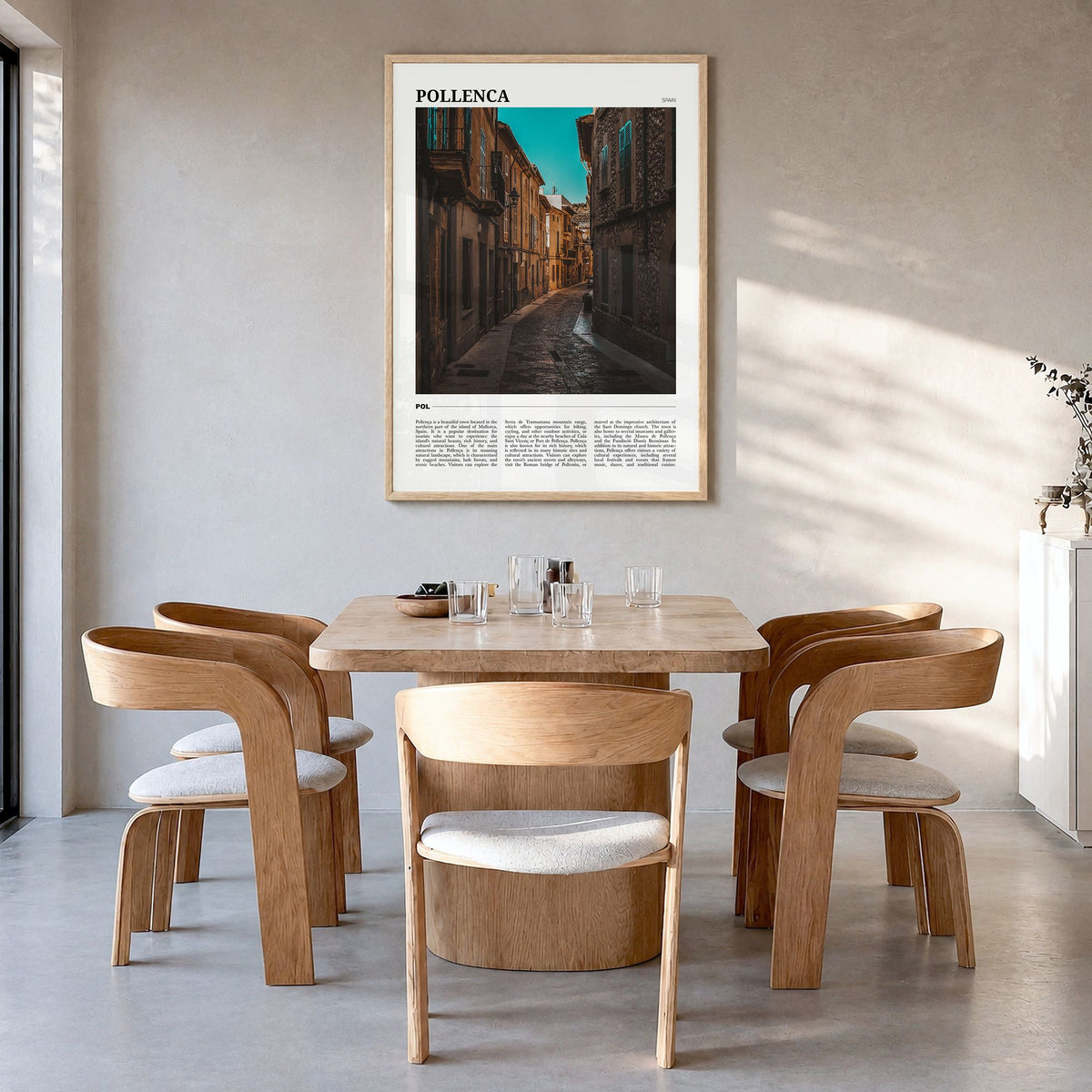 Pollença Travel Poster in a natural wood frame, hanging in a dining room